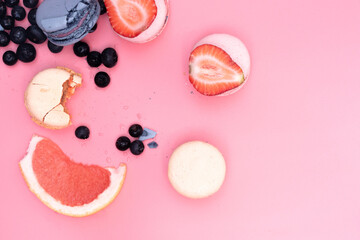 sweet Maroons are laid out in a circle decorated with pieces of strawberry and grapefruit and blueberries on a pink background