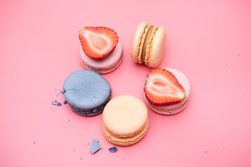 sweet Maroons are laid out in a circle decorated with strawberry slices on a pink background