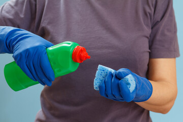 Woman holding a bottle of dishwashing liquid and a sponge on a blue background.