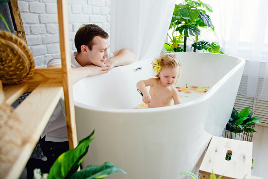 A cute little girl is sitting in a bath with milk and orange and yellow fruits and flowers. A young family spends time together. The concept of a family holiday. Bathing and playing with the child.