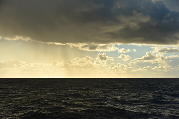 Seascape. It's raining over the horizon. Dark rain cloud and blue sky in the distance. 