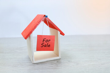 A toy house with for sale signage hanging 