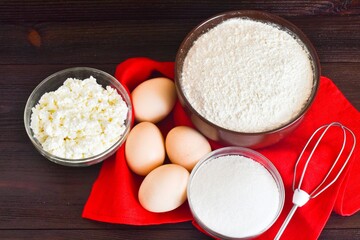 Ingredients for making curd pancakes. Flour, eggs, sugar, whisk, cottage cheese on a wooden brown...
