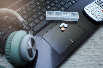 View of pills and pills container on the laptop, a headphone, and a calculator 
