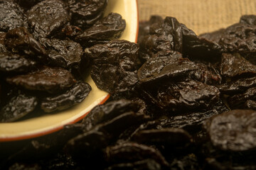 Dried prunes in a ceramic bowl and dried prunes scattered on a background of coarse-textured burlap. Close up.