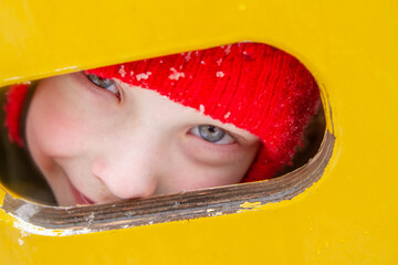 A little European boy with light blue eyes in a red hat looks out in winter. Close-up portrait of a child.