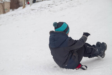 Fototapeta na wymiar A boy rides from a snow slide on a cardboard. Fun games in the snow.
