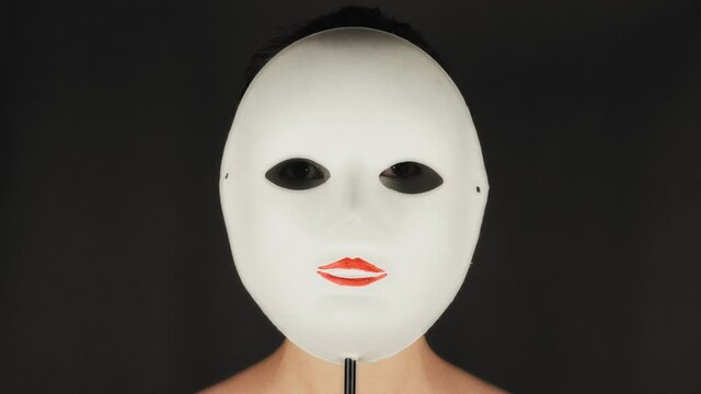 Brunette puts on a white theater mask. Theatrical makeup sad mask. Girl hides emotions behind a mask.
