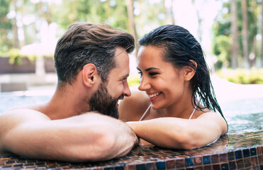 Cheerful couple in love are resting in a swimming pool while summer vacation.