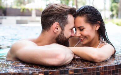Cheerful couple in love are resting in a swimming pool while summer vacation.