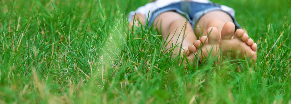 Children's Feet On The Green Grass In The Park. Selective Focus.