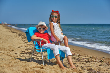 A brother and sister are relaxing on the seashore Two children are sitting on a beach chair on a deserted beach