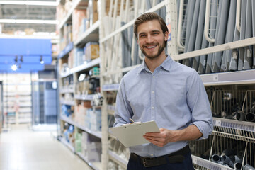 portrait of a smiling young warehouse worker working in a cash and carry wholesale store. - obrazy, fototapety, plakaty