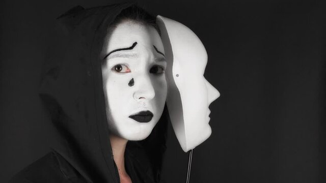 Brunette woman with white theatrical mask and make-up on her face. Sad girl takes off the theatrical mask from her face and looks at the camera. Hide emotions. High quality 4k footage