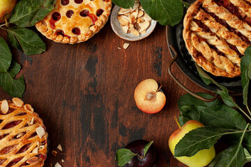 Homemade sweet pies with apples and plums on wooden background