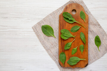 Fresh Baby Spinach on a rustic wooden board on a white wooden table, top view. Overhead, from above, flat lay. Copy space.