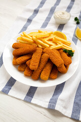 Homemade Fish Sticks and Fries with Tartar Sauce on a white wooden background, side view.
