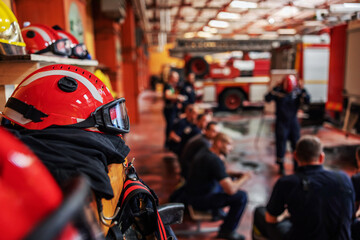 Obraz premium Closeup of firefighter sitting and listening boss who is talking about tactic how they gonna extinguish the fire. Fire brigade interior. Closeup of protective suit and helmet.