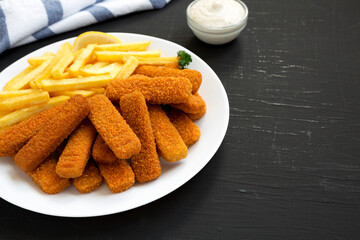 Homemade Fish Sticks and Fries with Tartar Sauce on a black background, side view. Copy space.