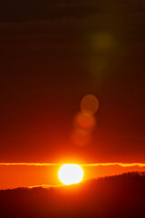 Rising of the sun in mountains, red-orange sun disk rises from tops of mountain range. Beautiful natural lens flare in orange sky, sunbeam light leaks.