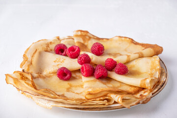 Thin pancakes with raspberries on a plate.