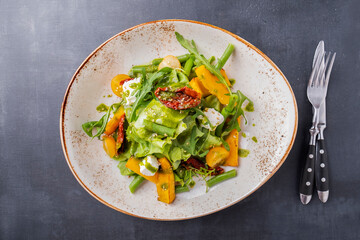Pumpkin salad with cheese and dried tomatoes on a plate served with fork and knife. Autumn salad. Top view