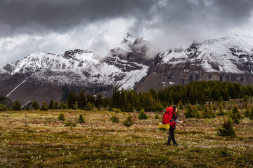Fototapeta na wymiar Female Backpacker Hiking in Canadian Rockies during a cloudy day. Taken near Banff, boarder of British Columbia and Alberta, Canada. Concept: Explore, Adventure, Trekking, Backpacking