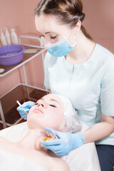Naklejka premium A beautician's office a woman beautician puts a brush rejuvenating mask on the face of an attractive client. Professional cosmetic services