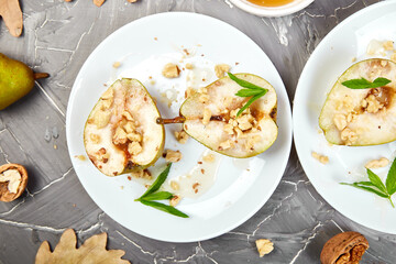 Tasty roast pears with honey and walnuts on white plates on grey background table. Top view.  Flat lay. Copy space.