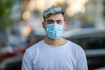 Handsome young man standing outdoors wearing medical mask to protect others from virus spread