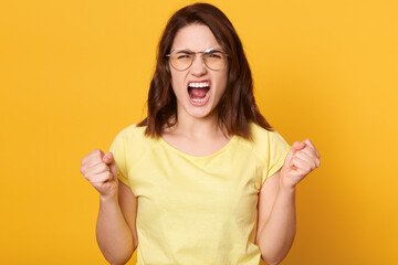 Angry young woman in glasses screaming with wild expression, being very upset, has dark hair,...