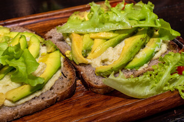 sandwich with hummus, sliced avocado and lettuce, vegetarian food, handmade food on a wooden tray