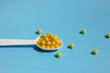 A white spoon filled with yellow vitamin C tablets on a blue background. Prevention of colds and flu