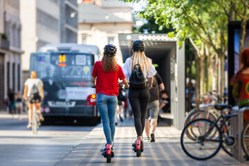Rear view of trendy fashinable teenager girls riding public rental electric scooters in urban city environment. New eco-friendly modern public city transport in Ljubljana, Slovenia.