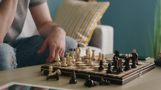 Wooden chess board with man-carved pieces is on the coffee table, man is playing chess alone, trying to kill time in self-isolation, Close up, Slow motion.