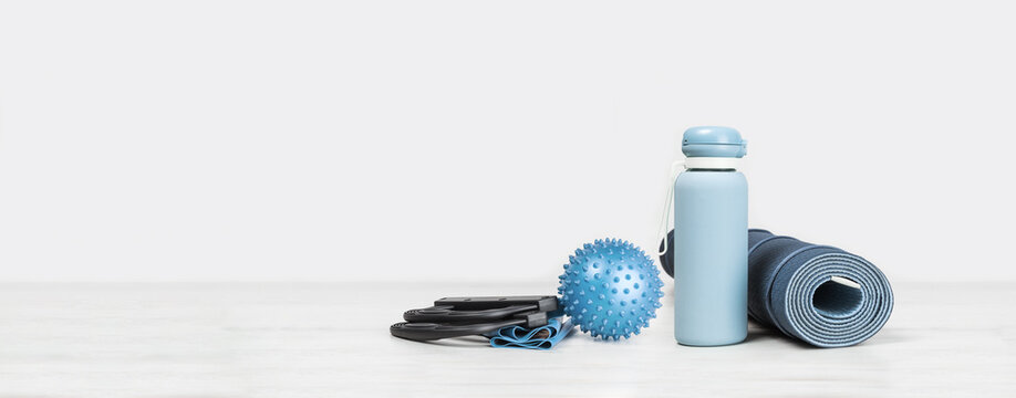 Rolled blue yoga mat. exercise resistance band water bottle on grey wooden surface. Gender neutral fitness and exercise concept with copy space. Active lifestyle. Workout at home or gym web banner