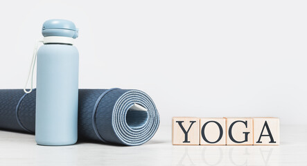 Rolled blue yoga mat and YOGA text on grey wooden surface. Blue water bottle Gender neutral fitness sport and exercise concept with copy space. Active lifestyle. Workout at home or gym