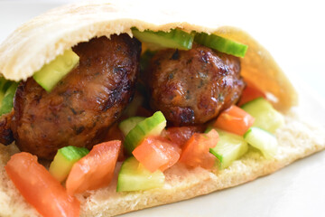 Sheftalia Cypriot Sausages with Fresh Vegetables (Cucumber and Tomato) on a White Plate. Traditional Cypriot food: Cypriot Lamb and Pork Sausages.  Copy space is on the blurry part. Selective focus.