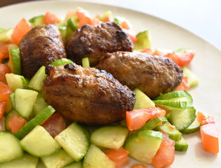 Sheftalia Cypriot Sausages with Fresh Vegetables (Cucumber and Tomato) on a White Plate. Traditional Cypriot food: Cypriot Lamb and Pork Sausages. Selective focus.  Copy space is on the blurry part.