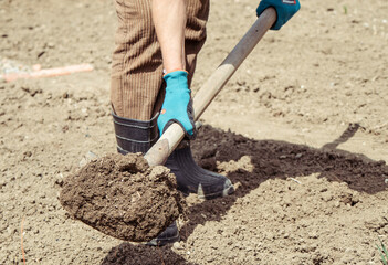 A woman cultivates land on a farm, part of the boots and the shovel can be seen