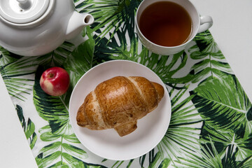 Classic breakfast in a white bowl on a trendy background with a herbal pattern. Croissant, herbal tea, green, flower, fruit, yogurt, apples, healthy, vegetarian.