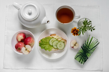 Breakfast in a white bowl on a light background croissant with herbs, vegetables, butter, cheese, herbal, green tea, flower, fruit, yogurt