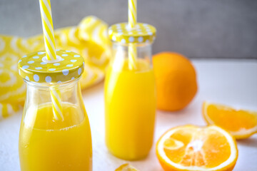 Freshly squeezed orange juice in glass bottles stands on a white table against the background of a gray wall. Near it lies a cut juicy orange. Diet and vegetarian concept, healthy food. Close-up