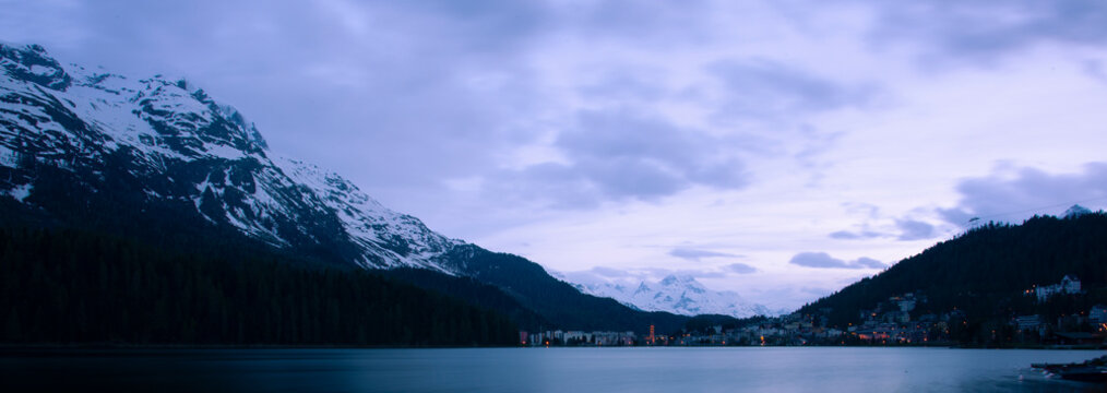 A night time panorama of the high alpine upscale resort town of St. Moritz, Switzerland. City lights, architecture, alpine summits, snow and lake view are seen. Image was taken across lake St. Moritz.