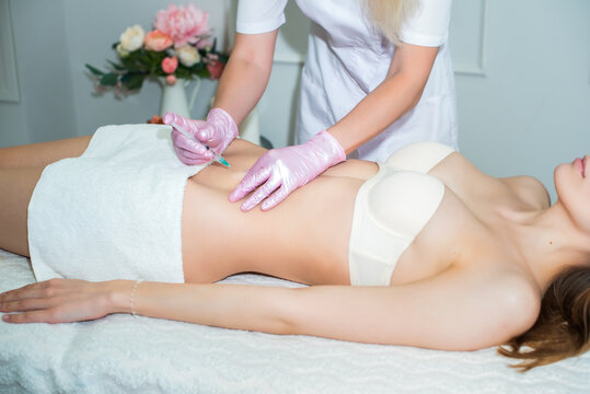 correction of body fat with lipolytics. female hands in pink gloves inject a young woman into the stomach.