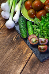 Green fresh washed wet vegetables on a table on a wooden background with copy space, healthy diet natural food and vitamin vegetarian organic food tomatoes, onions, leek cucumbers parsley