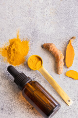 Fototapeta na wymiar Essential Turmeric oil in glass bottle, and turmeric roots and turmeric powder on light concrete background with copy space. Concept for alternative health care and wellness
