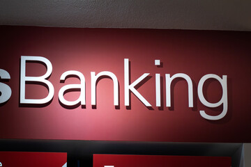 White sign saying Bank with light reflected onto it, with a red background.