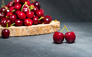 Primplan of two sweet cherries in light, in front of a stack of cherries on a wooden bottom, on black background.