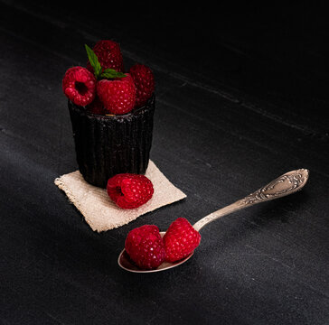 Raspberry on black backgound in a cup with
two raspberries in a teaspoon.